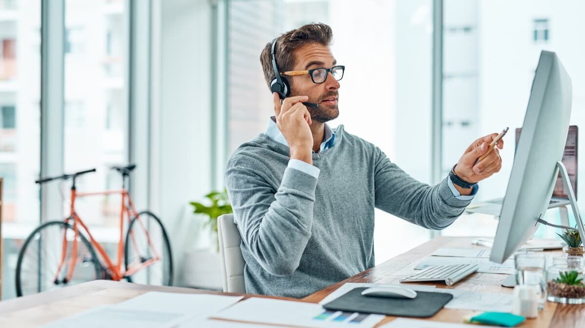 Mitarbeiter spricht mit Hilfe eines Headsets und zeigt währendessen auf dem Bildschirm seines Computers