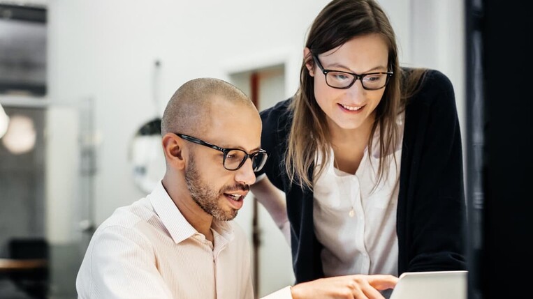 Männlicher Kollege und weibliche Kollgein schauen gemeinsam auf den Computer