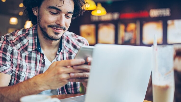 Mann mit Laptop und Smartphone im Café